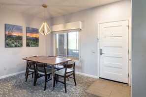 A dining area with a wooden table and chairs, a pendant light, and two wall-mounted paintings.