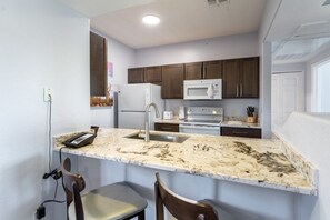 A kitchen with dark wooden cabinets, a white refrigerator, a microwave, and a granite countertop.
