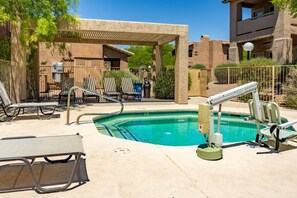 A pool area with lounge chairs, a covered seating area, and a poolside chair.