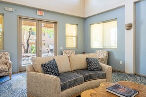 Un espace détente avec un canapé, des fauteuils et une table basse. De grandes fenêtres et un panneau indiquant la sortie sont présents.