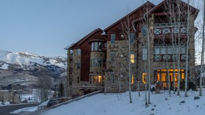 A large stone building with multiple windows and a balcony, surrounded by snow and trees. - Lorian #2 | Walk-Everywhere (Telluride)