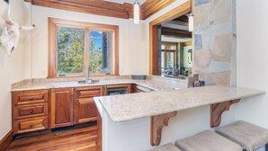 A kitchen with wooden cabinets, a granite countertop, a stone backsplash, and a window with a view of trees. - Lorian #2 | Walk-Everywhere (Telluride)