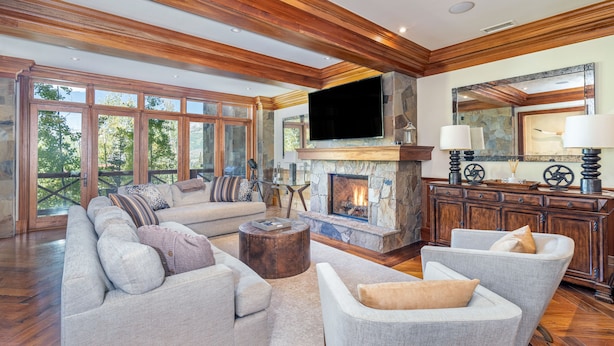 A spacious living room with a stone fireplace, wooden ceiling beams, and large windows offering a view of the outdoors. - Lorian #2 | Walk-Everywhere (Telluride)