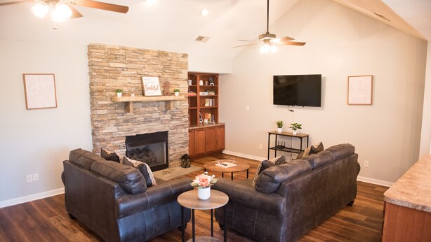 A living room with a stone fireplace, leather sofas, a coffee table, and a flat-screen TV mounted on the wall. - Peaceful 2-bedroom Townhome Just Steps Away from the Excitement of Pigeon Forge. (Pigeon Forge)