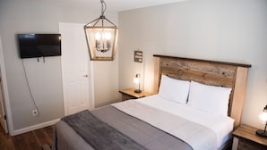 A bedroom with a bed, a television mounted on the wall, a wooden headboard, a nightstand with a lamp, and a door. - Peaceful 2-bedroom Townhome Just Steps Away from the Excitement of Pigeon Forge. (Pigeon Forge)