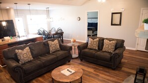 A modern living room with two dark brown sofas, a round coffee table, and a dining area in the background. - Peaceful 2-bedroom Townhome Just Steps Away from the Excitement of Pigeon Forge. (Pigeon Forge)