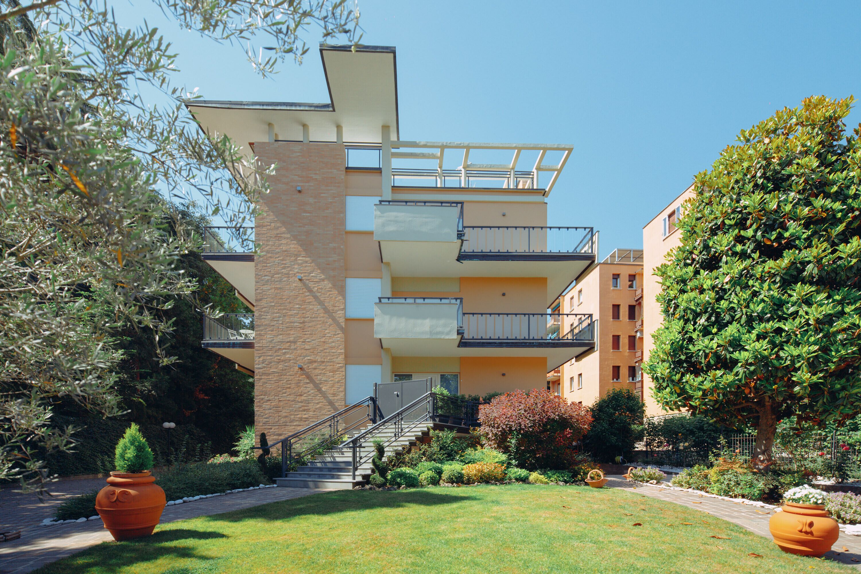 A multi-story building with balconies, a staircase, and a well-maintained garden with potted plants.