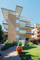 Un edificio residenziale a più piani con balconi, una scala centrale e un’area giardino curata.