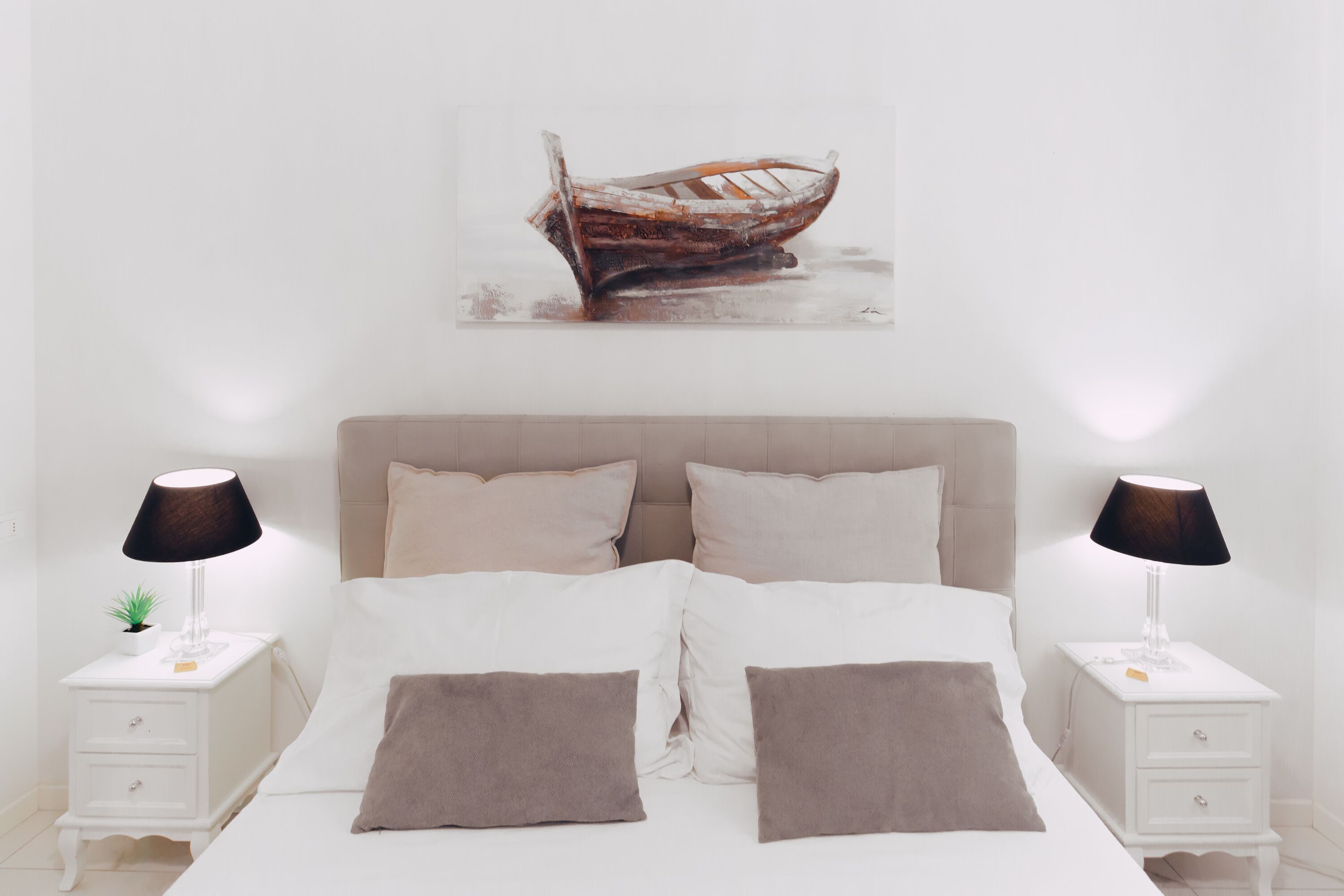 Ein Schlafzimmer mit einem Bett, zwei Nachttischen, einer Lampe und einem Gemälde eines Bootes an der Wand.