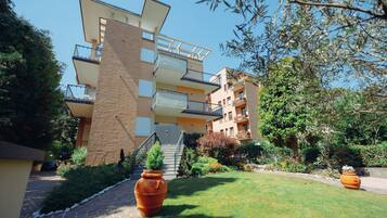 A multi-story residential building with balconies, a brick facade, and a well-maintained garden with large terracotta pots.