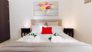 Un letto rifatto con cuscini bianchi e rossi, una coperta trapuntata color beige e due comodini con lampade.