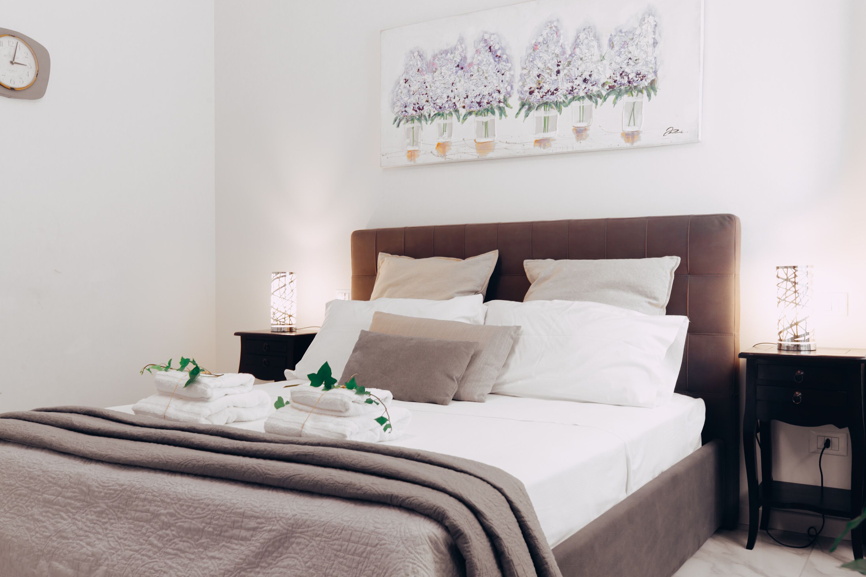 Una cama bien hecha con cabecera marrón, ropa de cama blanca y un cuadro decorativo encima.