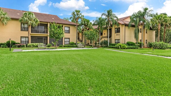 A residential building with a flat roof, multiple windows, and a well-maintained lawn with benches.
