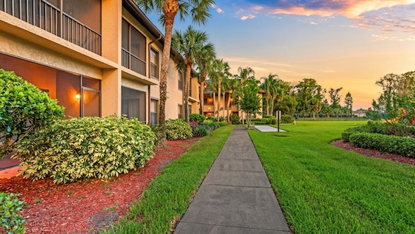 A pathway leading to a building with a modern design, surrounded by well-maintained greenery and palm trees.