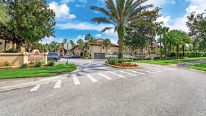 A gated community with multiple buildings, a pedestrian crossing, and a palm tree.