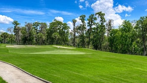 Ein Golfplatz mit blauem Himmel, gepflegtem Rasen und verschiedenen Bäumen im Hintergrund.