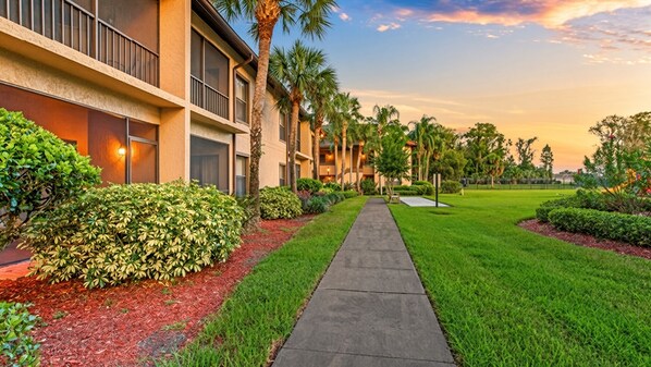 A pathway leading to a building with a modern design, surrounded by well-maintained greenery and palm trees.