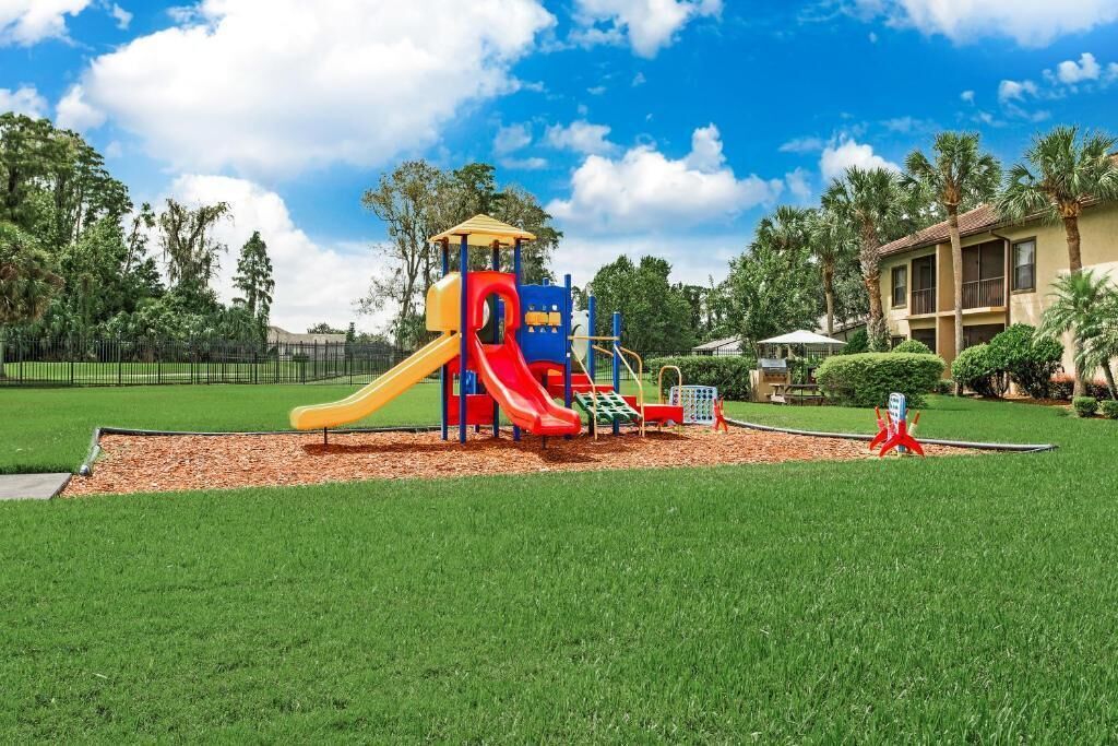 A playground with slides and climbing structures, surrounded by a well-maintained lawn and trees.