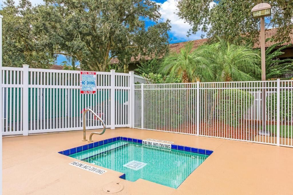 Une piscine entourée d’une clôture blanche, avec un panneau indiquant qu’il est interdit de plonger et un autre panneau affichant les règles de la piscine.