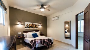 Una camera da letto con un letto, comodini, una ventola a soffitto, uno scaffale a parete con libri e uno specchio.