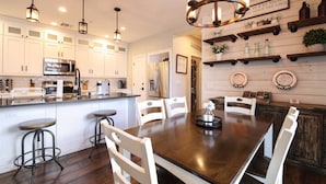 A modern kitchen with white cabinets, stainless steel appliances, and a wooden dining table with white chairs.
