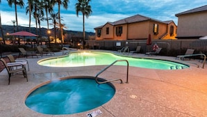 A swimming pool with a hot tub, lounge chairs, and palm trees.