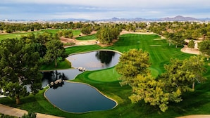 A golf course with multiple ponds, trees, and a distant cityscape.