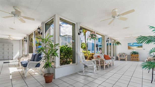 A spacious room with large windows, wicker furniture, and ceiling fans.