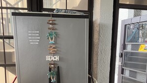 A compact, metallic refrigerator with a beach-themed decoration, located near a window and a door.