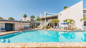 A swimming pool with lounge chairs and umbrellas, a shower area, and a building with a modern design.