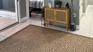 A living room with a flat-screen TV mounted on the wall, a wooden cabinet, and a patterned rug.