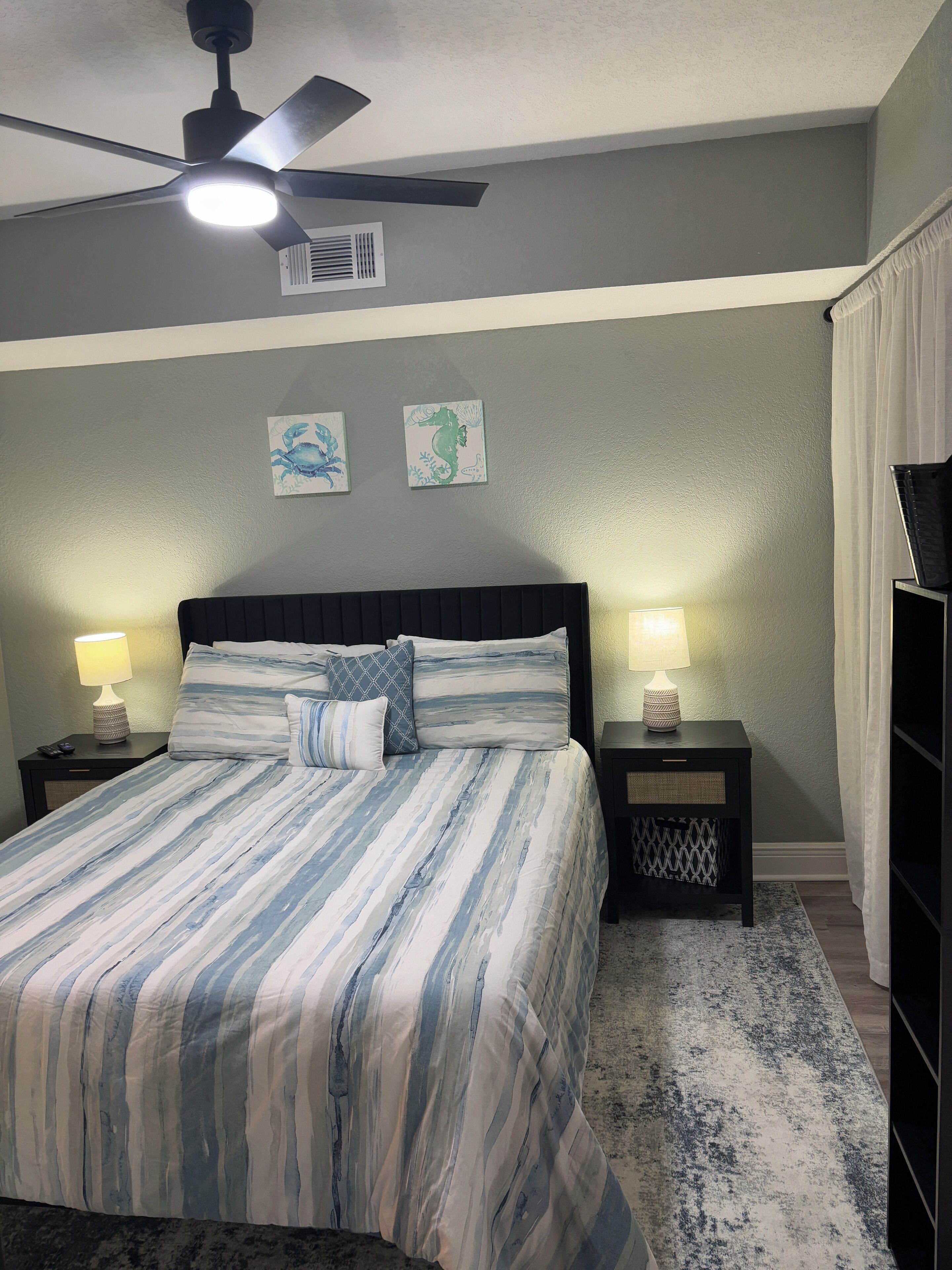 A bedroom with a bed, two bedside tables, a ceiling fan, and wall art.