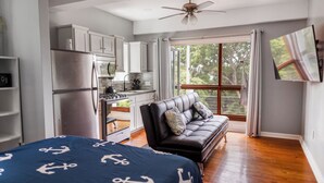 A modern bedroom with a bed, a sofa, a kitchen area, and a large window. - Gorgeous Entire Floor Condo - 3 BR Private Balcony & Rooftop Pool (West Bay)