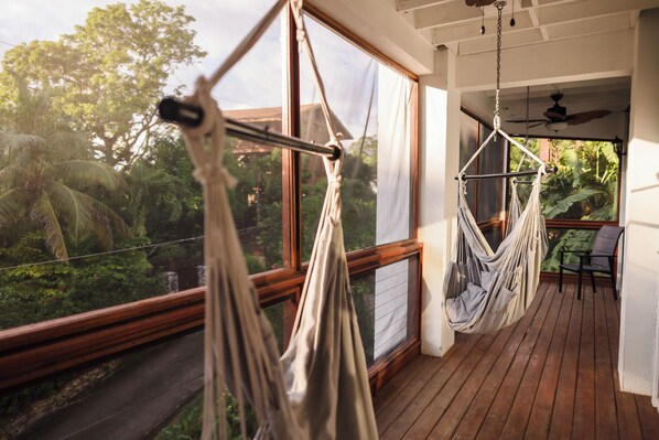 A wooden deck with two hammocks and a table, overlooking a lush garden.