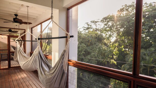 A hammock suspended from a ceiling fan in a room with large windows overlooking a forest. - Gorgeous Entire Floor Condo - 3 BR Private Balcony & Rooftop Pool (West Bay)