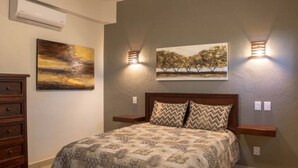 Ein Schlafzimmer mit einem Bett, zwei Wandleuchten, einem Gemälde, einer Kommode und einer Klimaanlage.