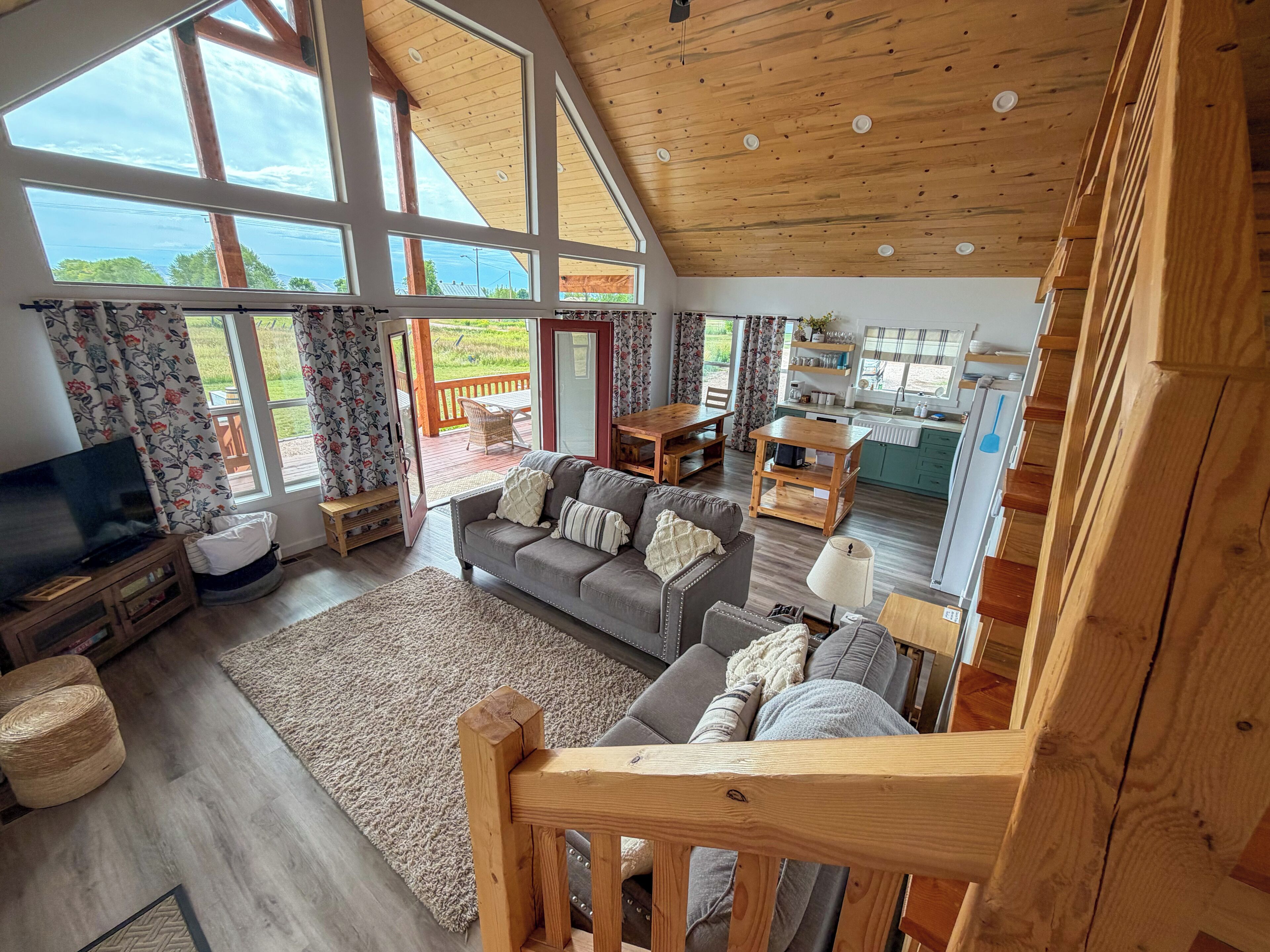 A spacious living area with a large window, a television, a sofa, and a wooden ceiling.