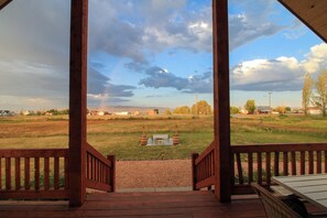 Une terrasse en bois offrant une vue sur un champ verdoyant et des bâtiments situés au loin.