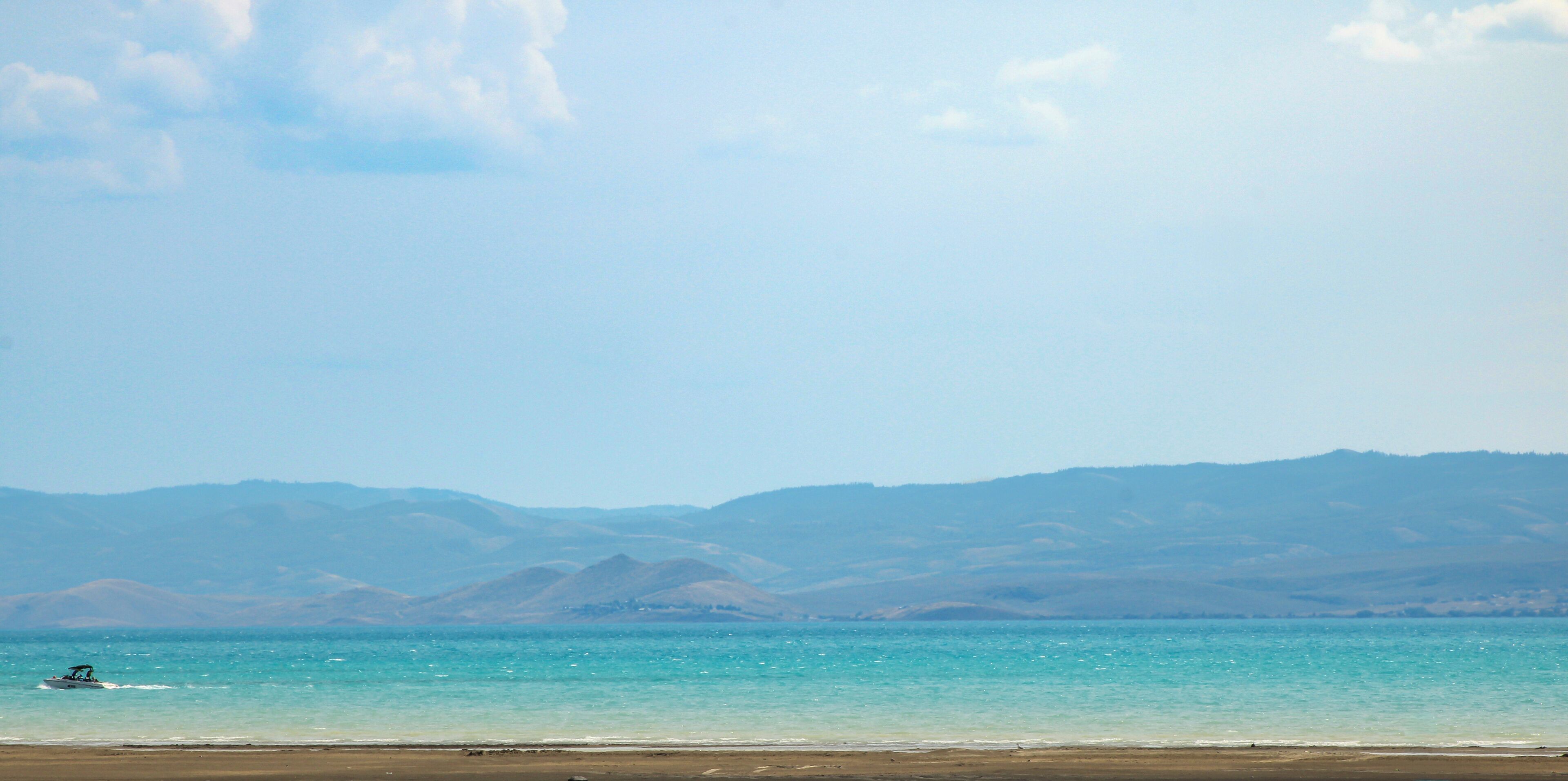 Une plage avec un bateau sur l’eau et des montagnes en arrière-plan.