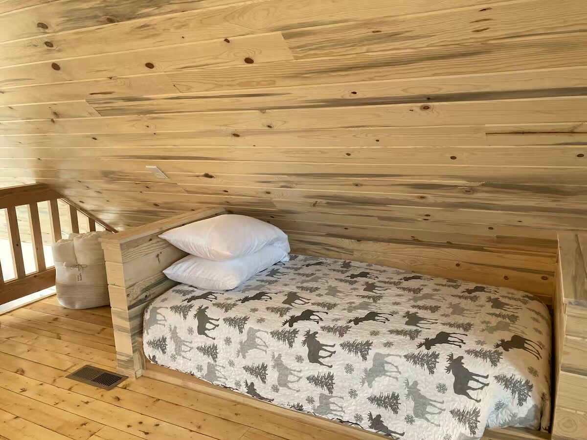 Una habitación de cabaña de madera con una cama, almohadas y un banco.
