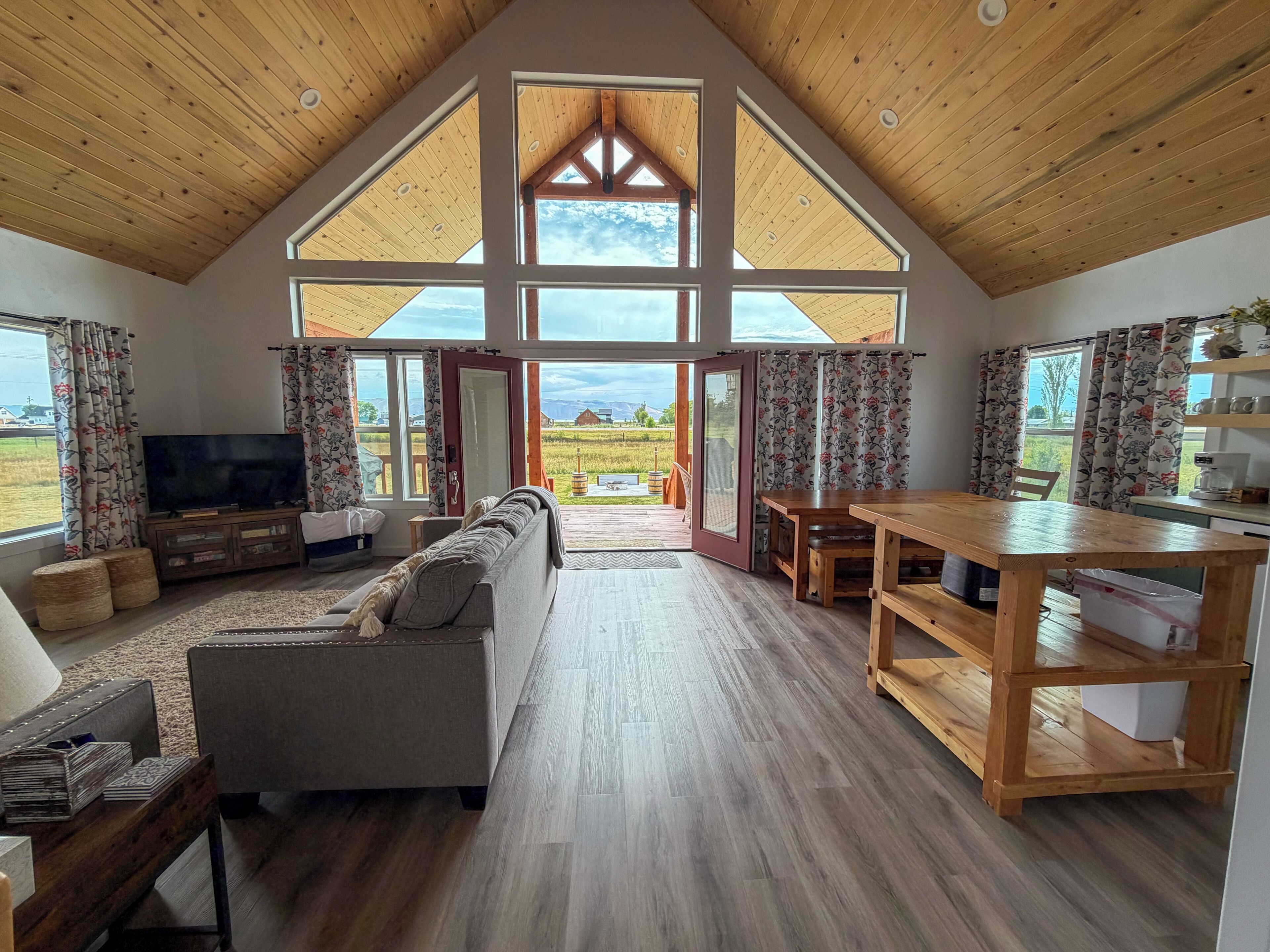 A spacious living area with a wooden ceiling, a large window, a sofa, a television, and a dining table.