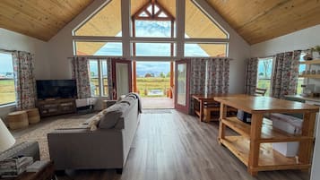 A spacious living area with a wooden ceiling, a large window, a sofa, a television, and a dining table.