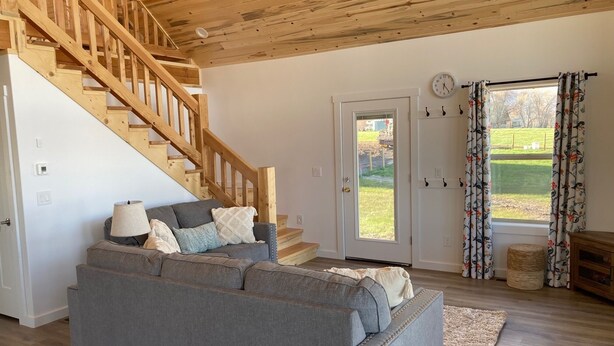 Ein Wohnzimmer mit grauem Sofa, einer Holztreppe und einer Tür, die nach draußen führt.