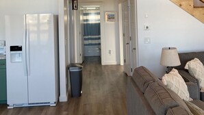 Ein geräumiger Wohnbereich mit Holzboden, einer Treppe, einer Küche mit Kühlschrank und einem Sofa mit Kissen.