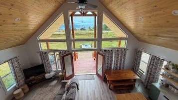 A spacious loft bedroom with a large skylight, a wooden ceiling fan, and a view of the countryside.