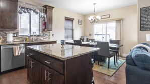 A modern kitchen with a granite island, dark wooden cabinets, and a dining area with a chandelier. - Sandy, UT home. Near the best skiing in the world (Sandy)
