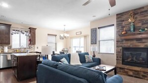 A modern living room with a blue sofa, a fireplace, and a kitchen area with wooden cabinets and a stone backsplash. - Sandy, UT home. Near the best skiing in the world (Sandy)