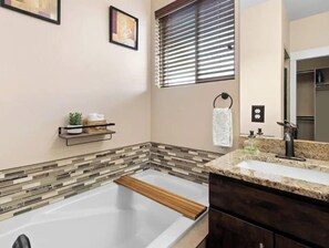 Une salle de bain moderne avec une grande baignoire, un meuble-lavabo avec un miroir et une fenêtre équipée de stores.