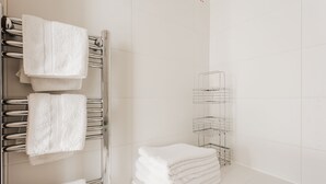 Ein Badezimmer mit Handtuchhalter, mehreren gefalteten Handtüchern, einer Metallregaleinheit und einem Fliesenboden.
