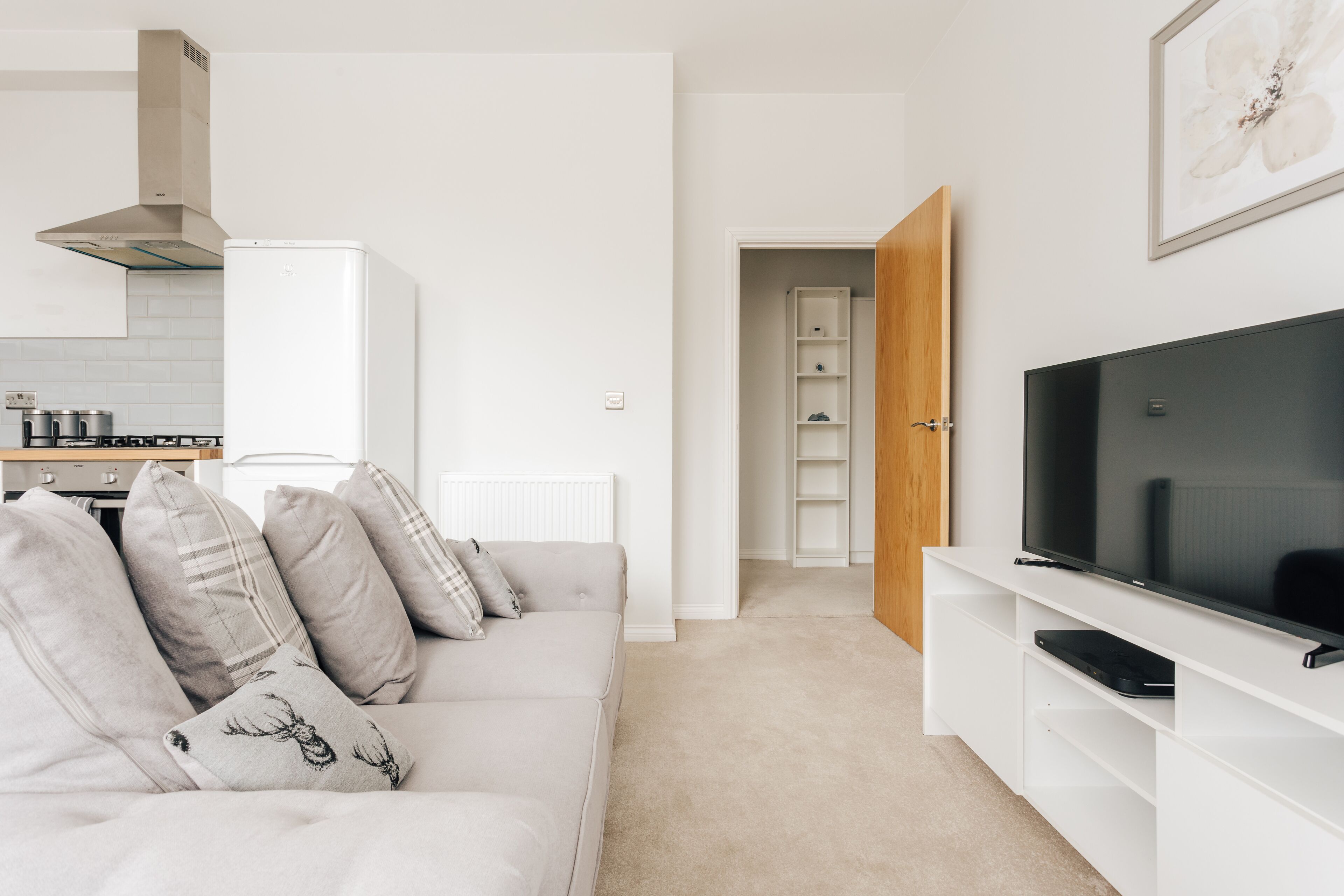 Una sala de estar moderna con un sofá blanco, un televisor de pantalla plana y una cocina al fondo.